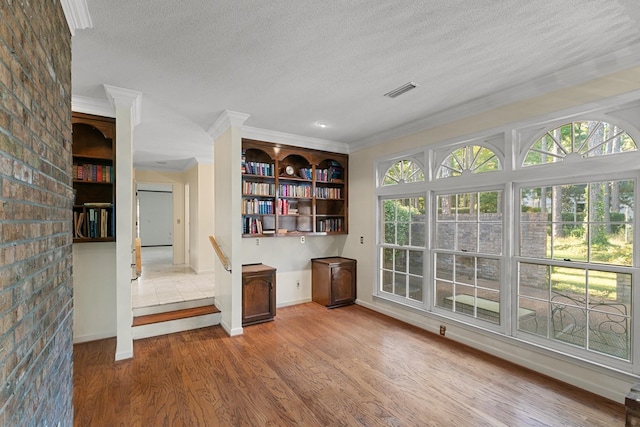 interior space featuring crown molding, wood finished floors, a textured ceiling, and a healthy amount of sunlight