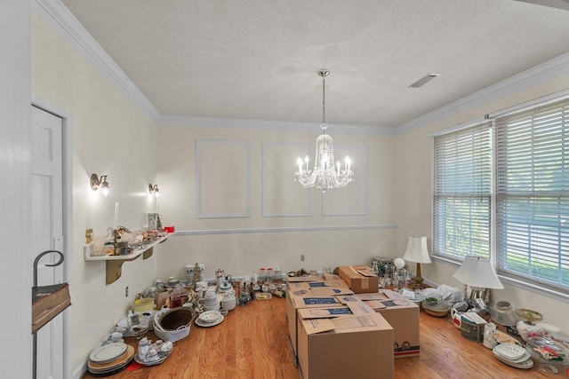 dining space with crown molding, a textured ceiling, visible vents, a chandelier, and wood finished floors