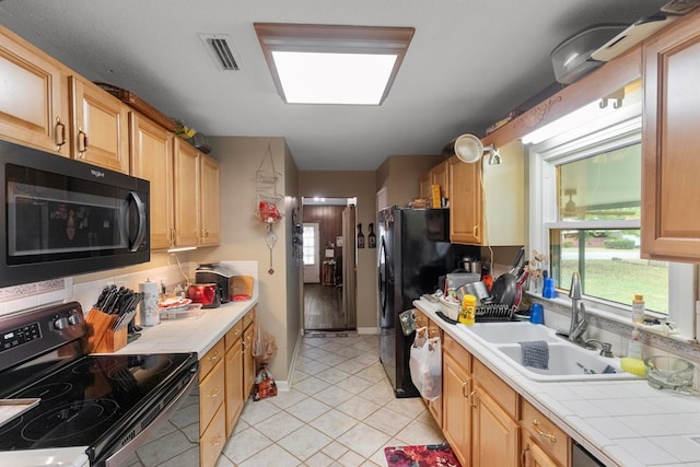 kitchen featuring black appliances, tile counters, light tile patterned floors, and sink