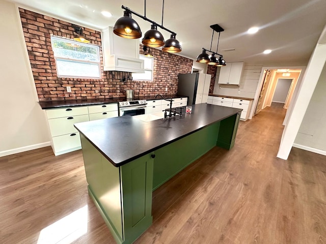 kitchen with appliances with stainless steel finishes, white cabinets, a kitchen island with sink, and brick wall