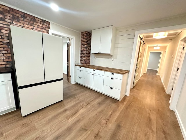 kitchen with light wood-type flooring, butcher block countertops, white cabinetry, and brick wall