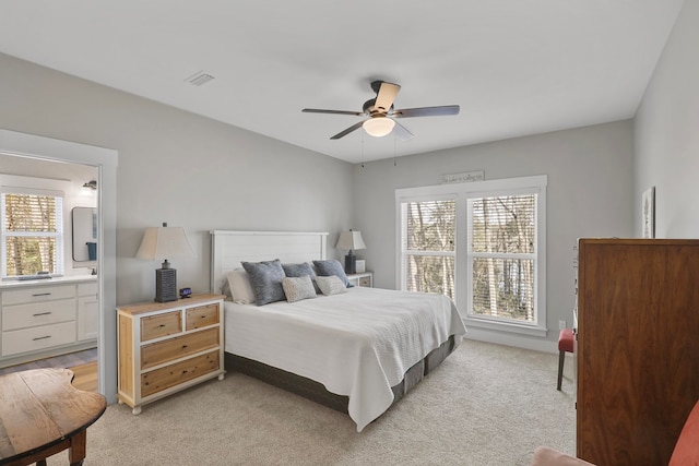 bedroom with multiple windows, light carpet, ceiling fan, and ensuite bath