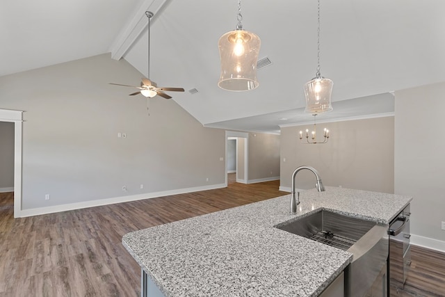 kitchen with dark hardwood / wood-style floors, light stone counters, hanging light fixtures, and an island with sink