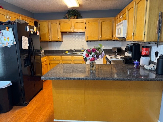 kitchen with light wood-type flooring, white appliances, a peninsula, a textured ceiling, and a sink