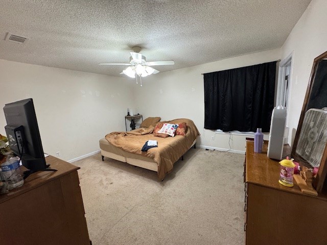 bedroom with baseboards, a textured ceiling, a wood stove, ceiling fan, and carpet