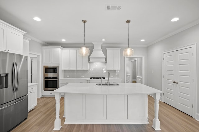 kitchen with sink, premium range hood, hanging light fixtures, stainless steel appliances, and white cabinets