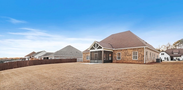 rear view of property with central AC, a sunroom, and a lawn