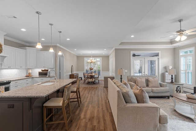 living room with ceiling fan with notable chandelier, crown molding, dark hardwood / wood-style flooring, and sink