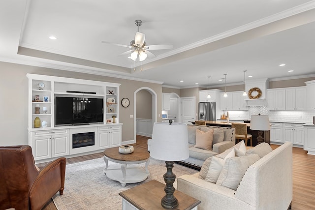 living room with ceiling fan, a tray ceiling, crown molding, and light hardwood / wood-style flooring