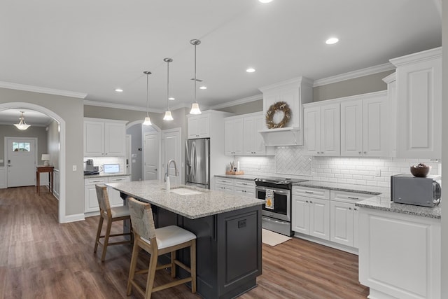 kitchen featuring appliances with stainless steel finishes, white cabinetry, a kitchen island with sink, and light stone counters