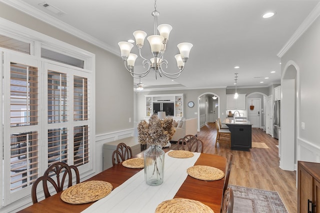 dining space featuring sink, an inviting chandelier, ornamental molding, and light hardwood / wood-style flooring