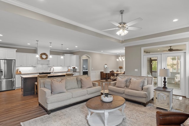 living room featuring ceiling fan with notable chandelier, hardwood / wood-style flooring, crown molding, and sink