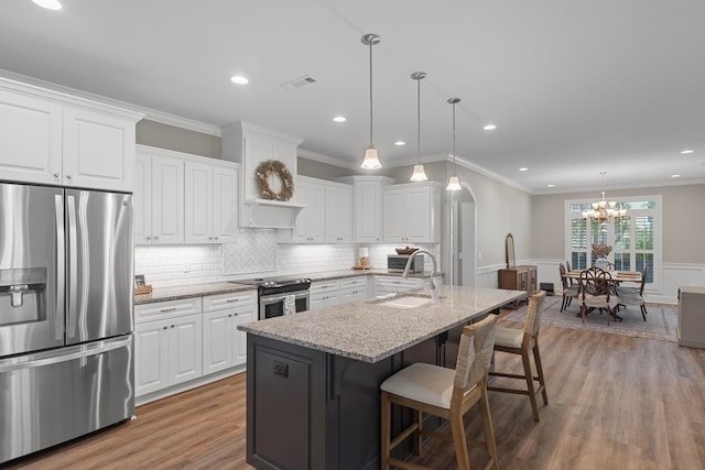 kitchen with stainless steel appliances, decorative light fixtures, white cabinetry, an island with sink, and light stone countertops