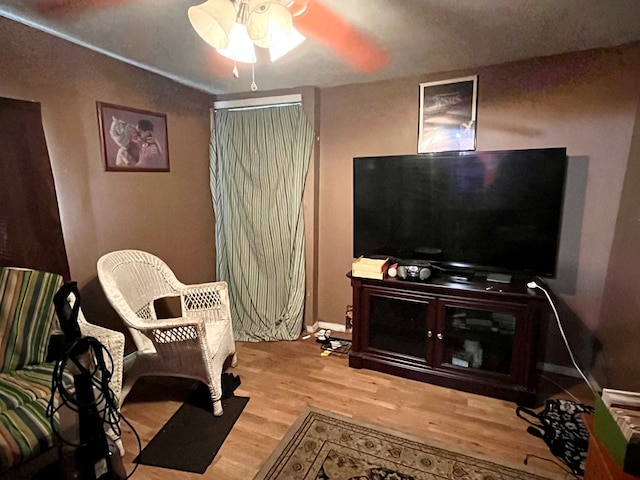 living area with wood finished floors, a ceiling fan, and baseboards