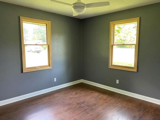 empty room with a textured ceiling, ceiling fan, a healthy amount of sunlight, and dark wood-type flooring