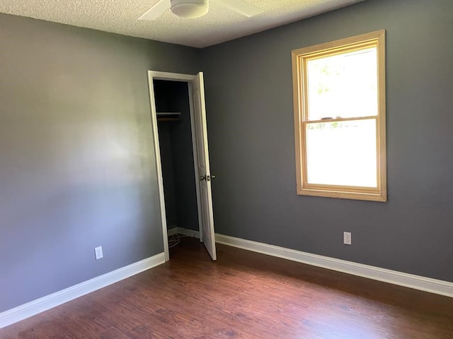 unfurnished bedroom with ceiling fan, a closet, dark wood-type flooring, and a textured ceiling