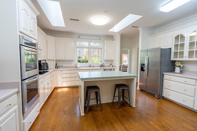 kitchen featuring a skylight, ornamental molding, stainless steel appliances, white cabinets, and a kitchen island