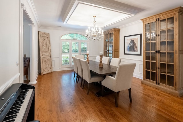 dining area with ornate columns, an inviting chandelier, hardwood / wood-style floors, a tray ceiling, and ornamental molding