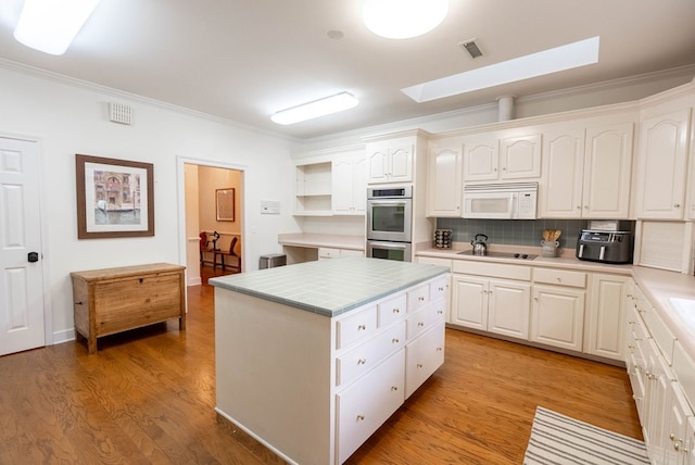 kitchen with black electric stovetop, ornamental molding, stainless steel double oven, a kitchen island, and white cabinetry