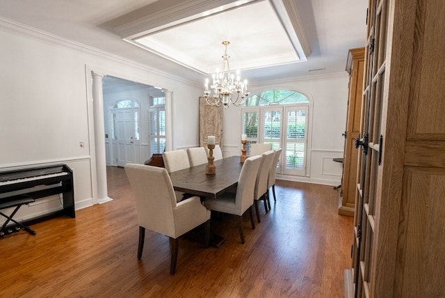 dining area featuring ornate columns, a raised ceiling, dark hardwood / wood-style floors, a notable chandelier, and ornamental molding