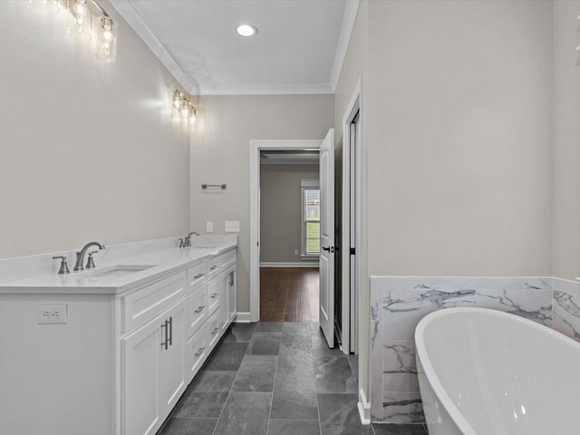 bathroom with a freestanding tub, ornamental molding, double vanity, recessed lighting, and baseboards