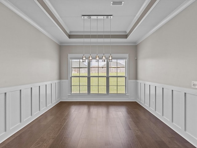 unfurnished dining area featuring a raised ceiling, dark wood finished floors, a wainscoted wall, a chandelier, and ornamental molding