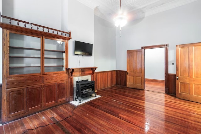 unfurnished living room featuring a wood stove, ceiling fan, a high ceiling, hardwood / wood-style flooring, and ornamental molding