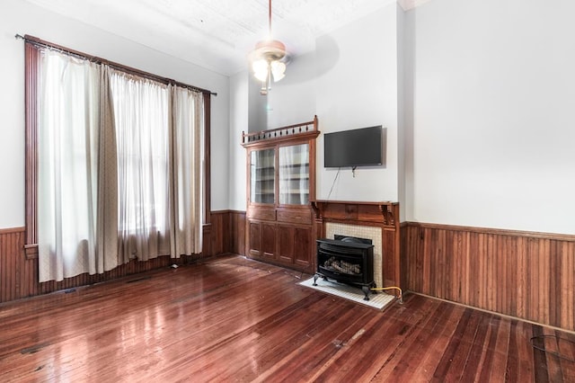 unfurnished living room featuring wood-type flooring, a wood stove, ceiling fan, and wood walls