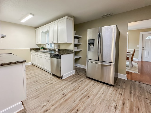 kitchen with white cabinetry, sink, dark stone counters, light hardwood / wood-style floors, and appliances with stainless steel finishes