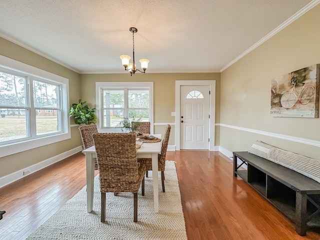 dining room featuring light wood-type flooring, a textured ceiling, an inviting chandelier, and crown molding