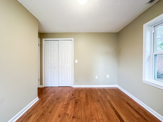 unfurnished bedroom featuring wood-type flooring, a textured ceiling, and a closet