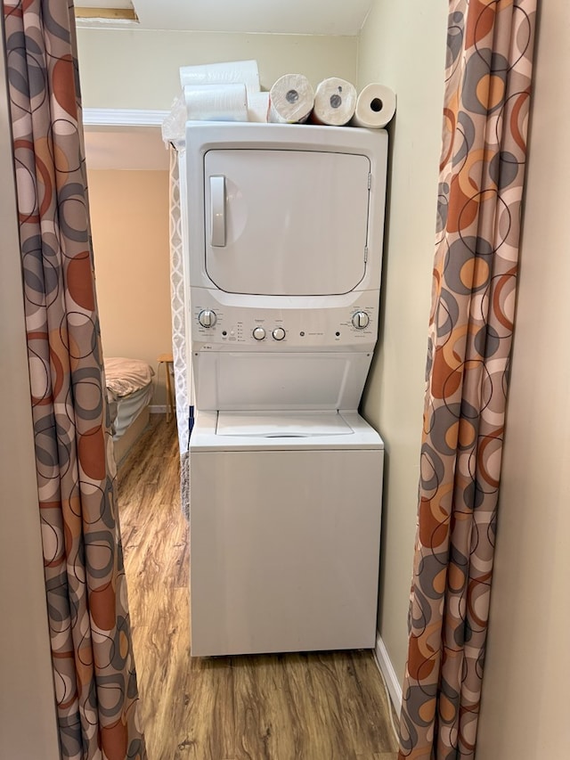 clothes washing area featuring hardwood / wood-style flooring and stacked washer / drying machine