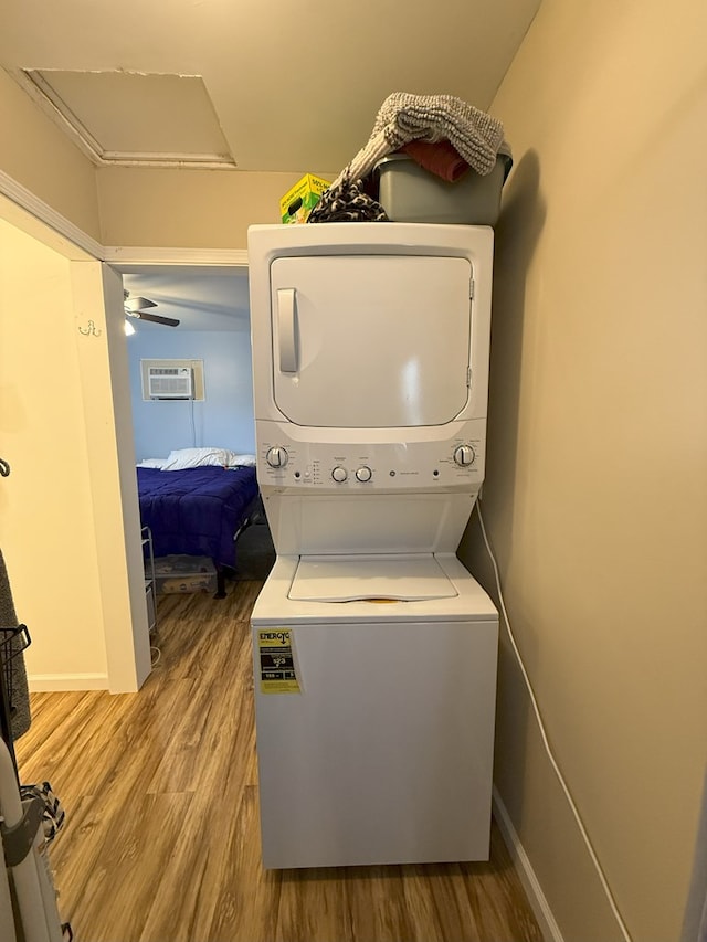 laundry room featuring stacked washing maching and dryer, a wall mounted air conditioner, and light wood-type flooring