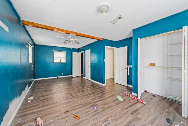 unfurnished bedroom featuring beam ceiling, ceiling fan, wood-type flooring, and a textured ceiling