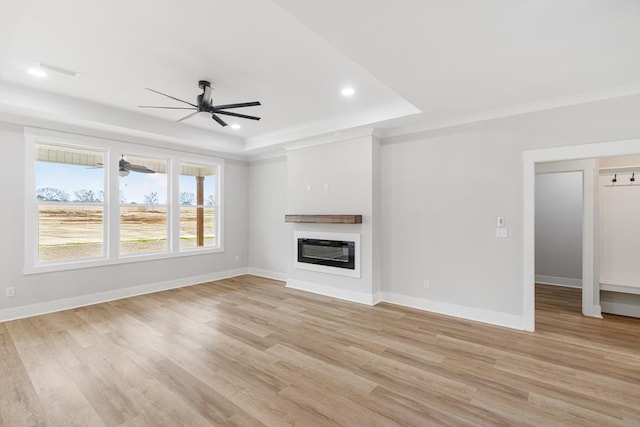 unfurnished living room featuring a tray ceiling, ornamental molding, ceiling fan, and light wood-type flooring