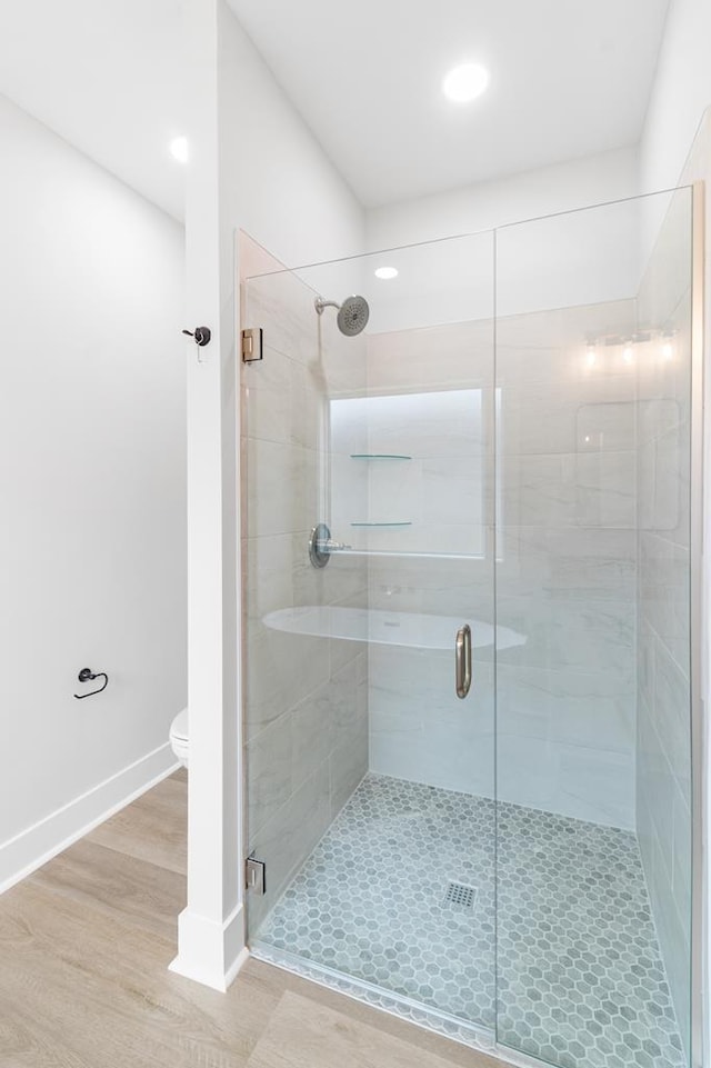 bathroom featuring hardwood / wood-style flooring, a shower with door, and toilet