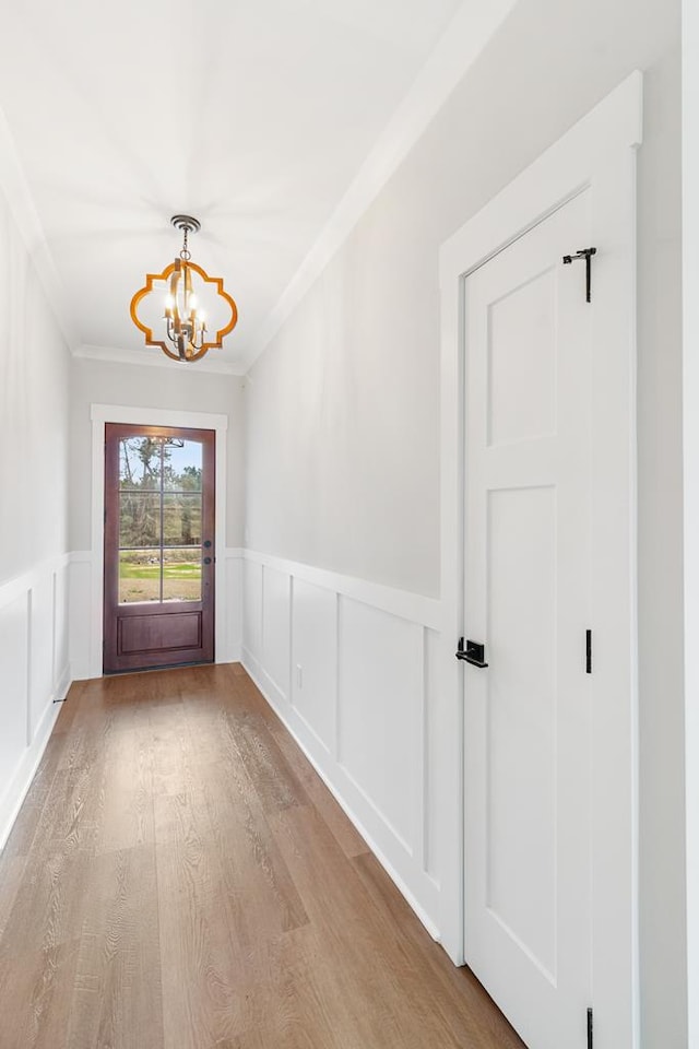 doorway with crown molding, a chandelier, and light hardwood / wood-style flooring