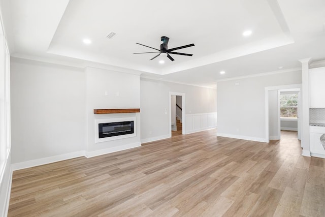 unfurnished living room with light hardwood / wood-style flooring, ornamental molding, a raised ceiling, and ceiling fan