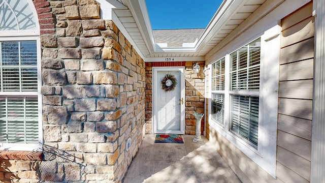 property entrance with a shingled roof and stone siding