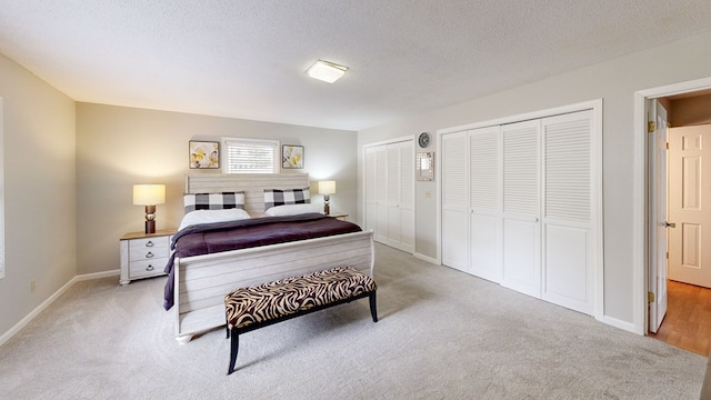 bedroom with a textured ceiling, baseboards, light colored carpet, and multiple closets