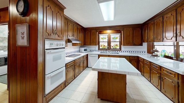 kitchen featuring light tile patterned floors, tasteful backsplash, a kitchen island, a sink, and white appliances