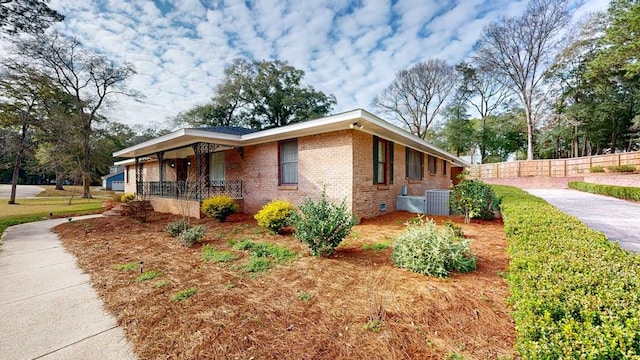 view of side of property featuring central AC unit, crawl space, fence, a porch, and brick siding