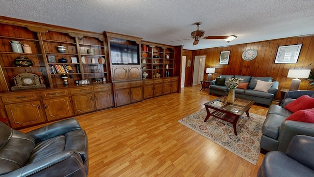 living room with wood walls, ceiling fan, light wood-type flooring, and a textured ceiling