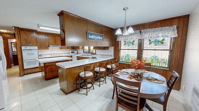 kitchen featuring a chandelier, under cabinet range hood, a peninsula, white appliances, and a sink