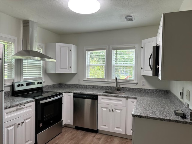 kitchen featuring wall chimney exhaust hood, stainless steel appliances, sink, white cabinets, and light hardwood / wood-style floors