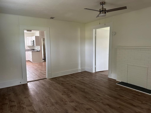 unfurnished room featuring ceiling fan, dark hardwood / wood-style floors, and a brick fireplace