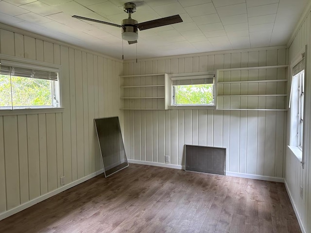 spare room featuring wood-type flooring, wooden walls, ceiling fan, and a healthy amount of sunlight