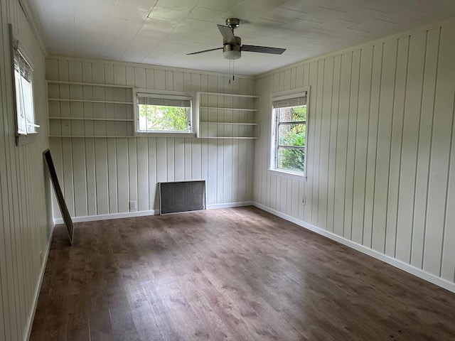 unfurnished room with wood walls, a healthy amount of sunlight, dark hardwood / wood-style flooring, and built in features