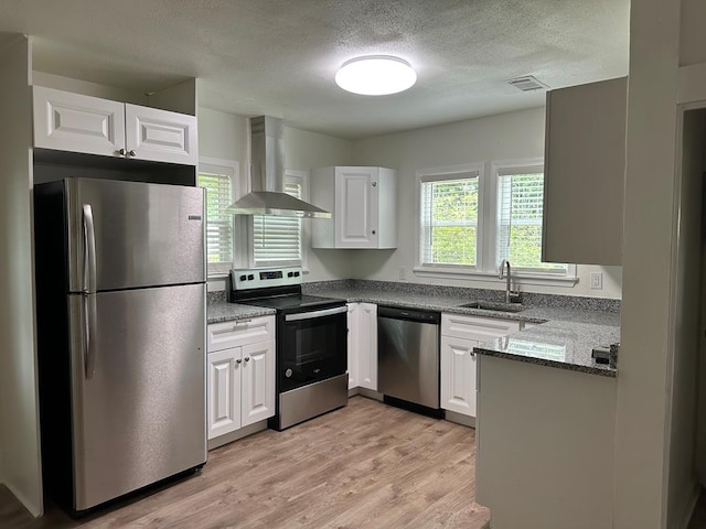 kitchen featuring appliances with stainless steel finishes, light wood-type flooring, wall chimney exhaust hood, sink, and white cabinets