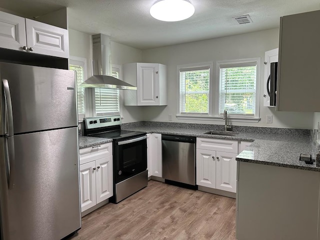 kitchen with white cabinets, wall chimney range hood, sink, light hardwood / wood-style floors, and stainless steel appliances